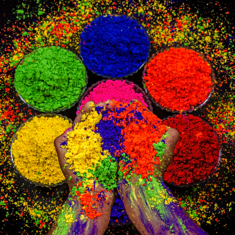 Holi context picture featuring colored powders in primary colors and a hand holding the,
