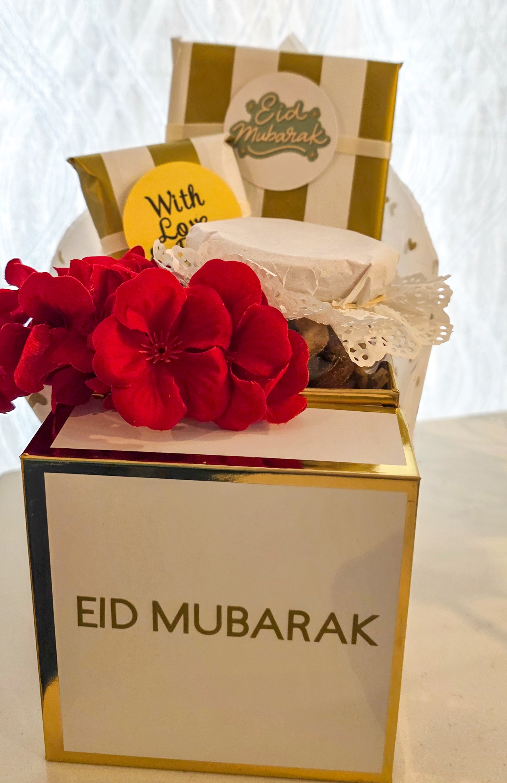 Gift box with 'Eid Mubarak' text, red flowers, and a striped bag on a white background